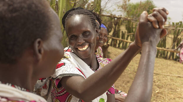 Frauen aus Kenia schlagen freudig ein, eine strahlt dabei in die Kamera.