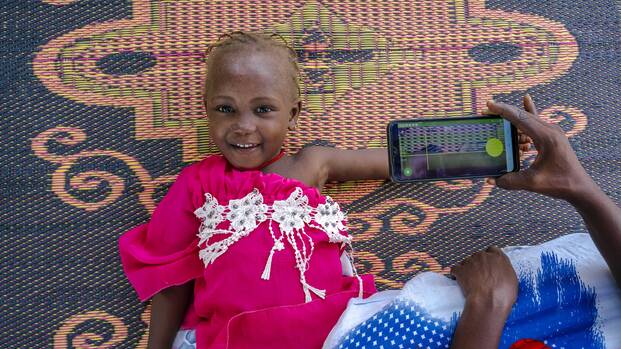 Ein Mädchen liegt lächelnd auf einem Teppich, während eine Frau ihren Arm mithilfe der SAM Photo App fotografiert. Ein Mädchen liegt lächelnd auf einem Teppich, während eine Frau ihren Arm mithilfe der SAM Photo App fotografiert.