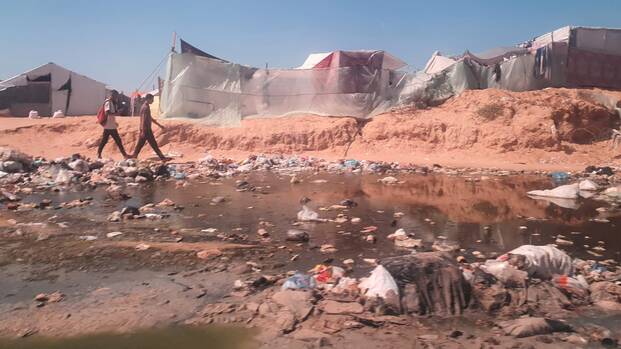 Zwei Jugendliche laufen an einer zerstörten Zeltstadt in Gaza vorbei.