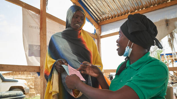 Eine Mitarbeiterin gibt einer Frau aus dem Tschad Bescheinigungen.