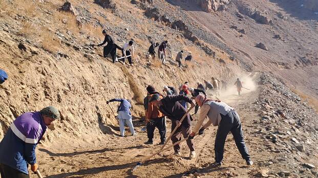 Unsere lokalen Teams in Afghanistan arbeiten mit Schaufeln und Rechen an der Befestigung einer Straße, die durch das Hochland von Daykundi führt.