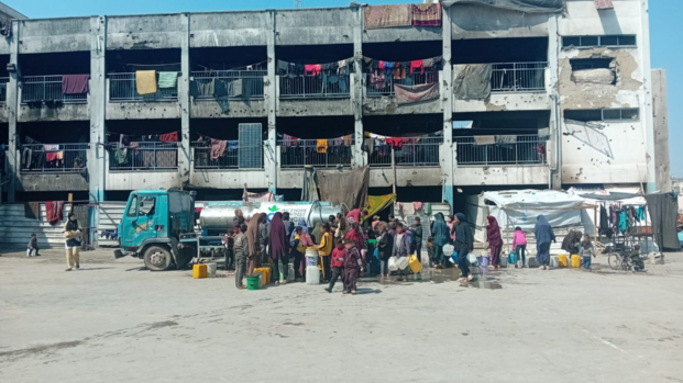 Menschen in Gaza stehen vor einem beschädigten Gebäude für Trinkwasser an.