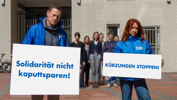 Mitarbeiter*innen von Aktion gegen den Hunger mit Protestschildern "Solidarität nicht kaputtsparen!" und "Kürzungen stoppen"