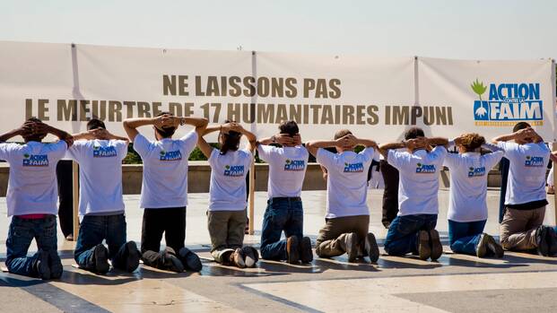 Kniende Mitarbeiter*innen von Aktion gegen den Hunger zum Gedenken an das ungesühnte Massaker an 17 humanitären Helfer*innen